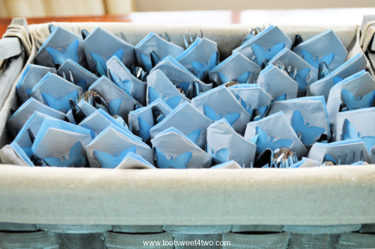 blue and gray paper napkins rolled with utensils in a gray basket