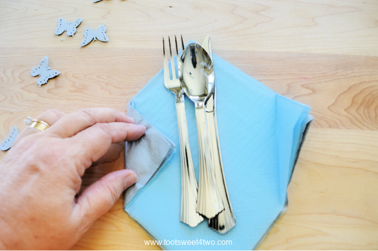 folding paper napkins inward to bundle the plastic silverware