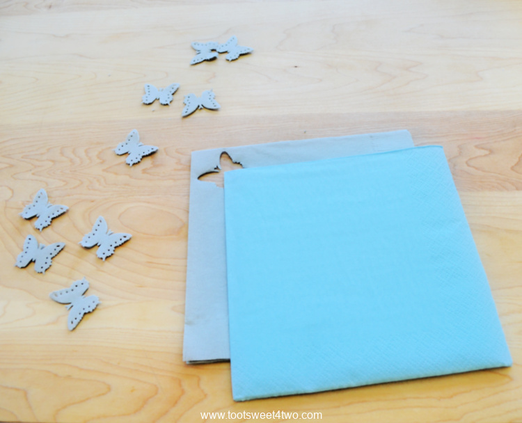 gray paper napkin with butterfly punched out and a blue paper napkin