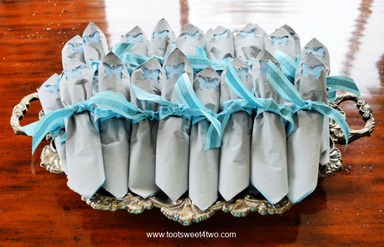 a bunch of gray and blue paper napkins folded with silverware inside tied with blue ribbon