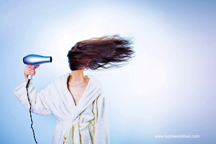 Funny woman in bathrobe blowing hair with hairdryer