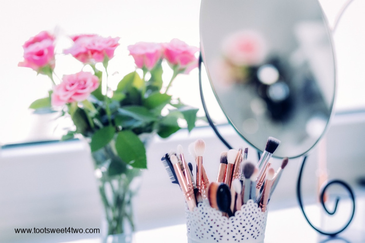 Makeup brushes in a container and makeup mirror and a vase of roses