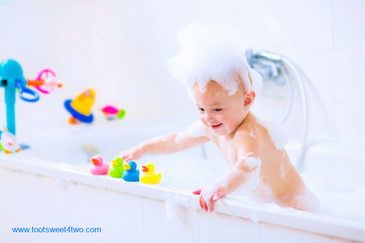 baby in bath tub full of bubbles and bath toys