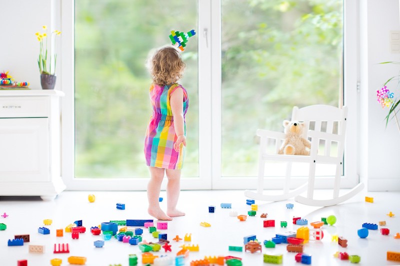 Cute toddler girl playing with colorful blocks, building an airplane in a sunny bedroom with a big window