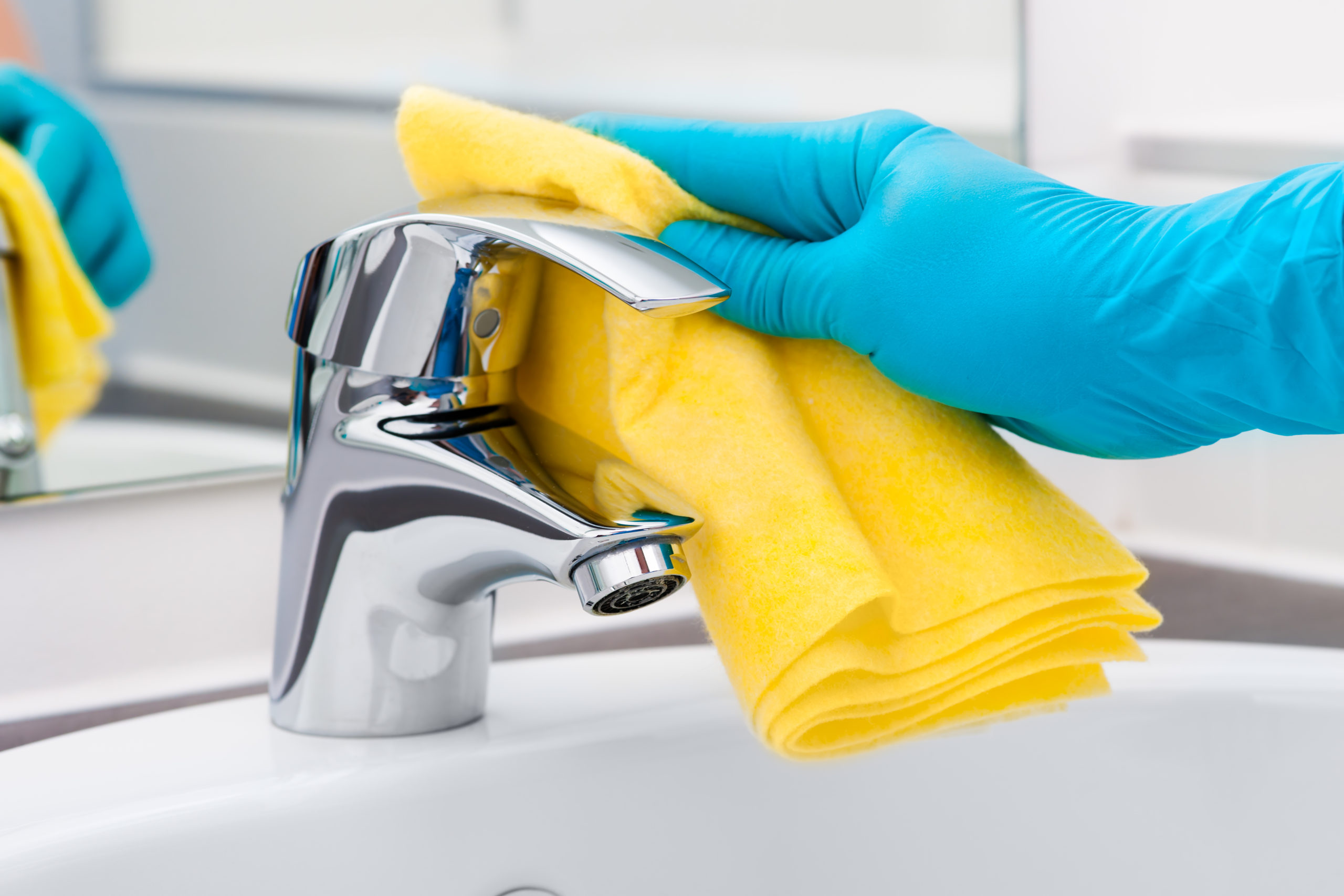 Person wearing gloves cleaning bathroom faucet