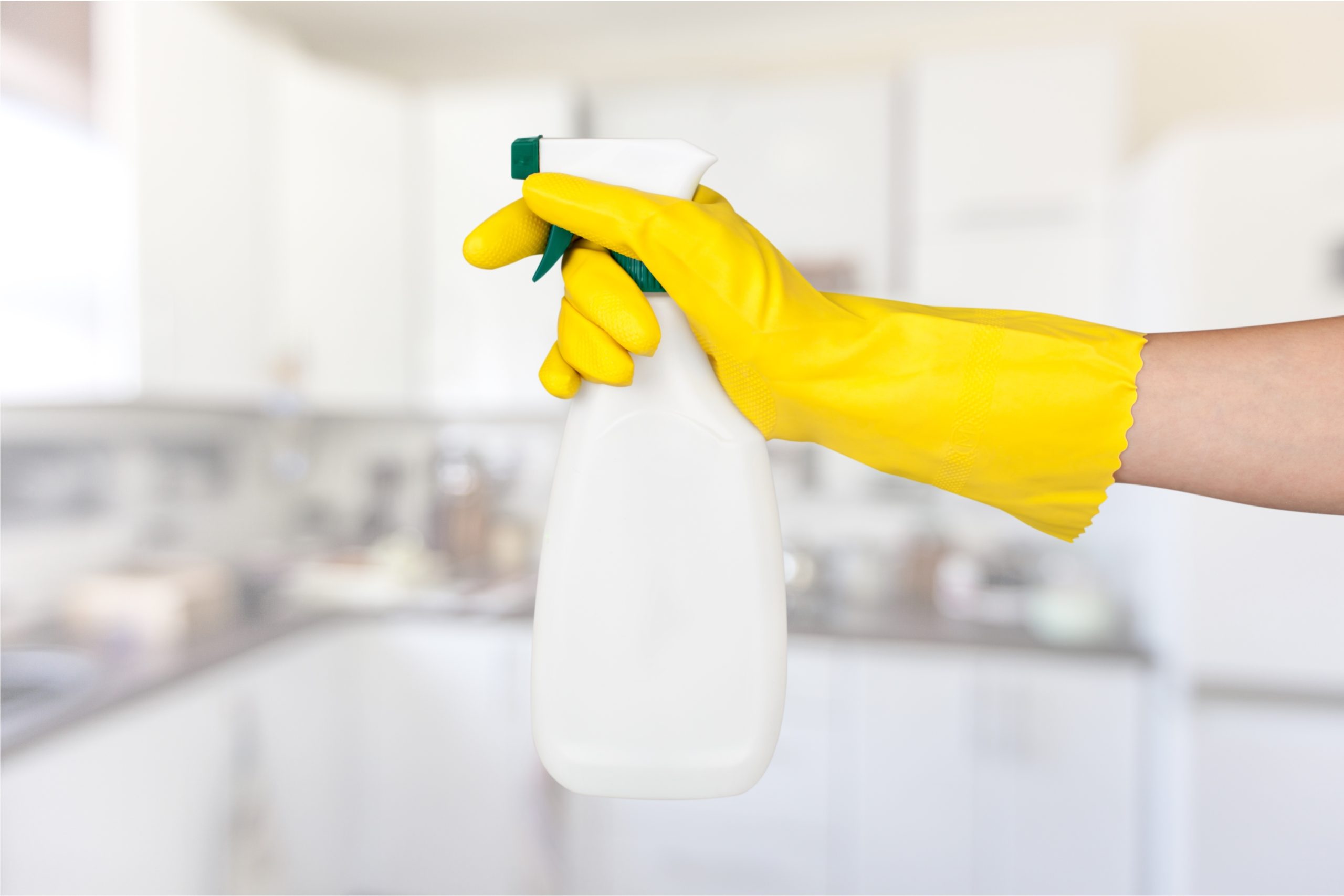 Person wearing gloves holding spray bottle in kitchen