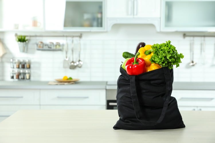Textile shopping bag full of vegetables on table in kitchen.