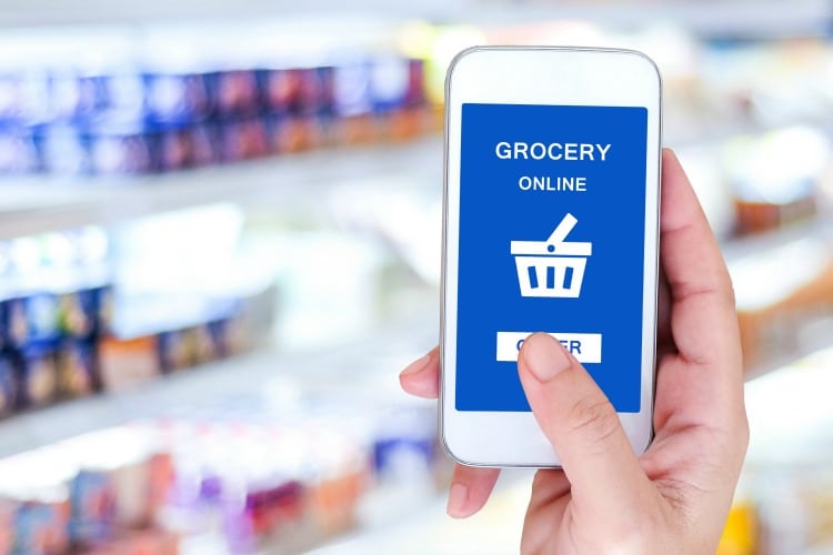 Hand holding smart phone with grocery shopping online on screen over blur supermarket background, retail business and technology concept