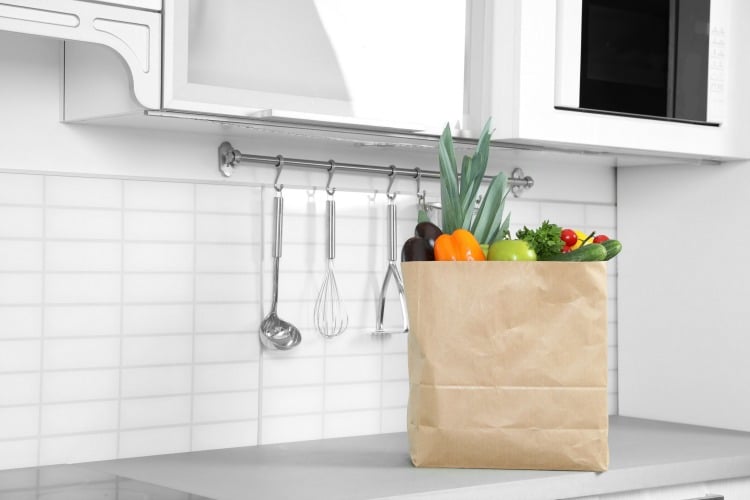Paper shopping bag full of vegetables on countertop in kitchen.